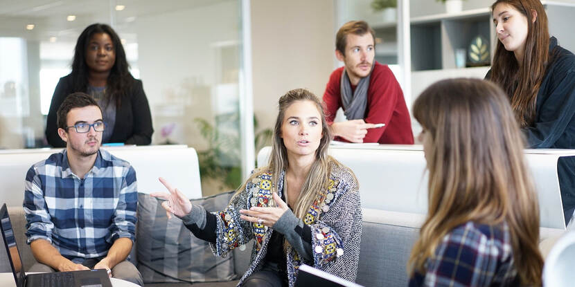 6 mensen zijn in gesprek met elkaar. Er staat een laptop in het midden op tafel